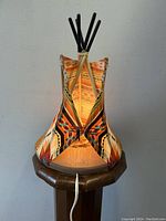 Front view of the illuminated teepee table lamp showing warm light inside and detailed geometric fabric patterns.