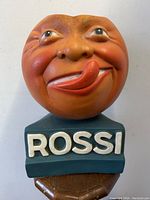 Front view showing orange moon face and white “ROSSI” lettering on teal base