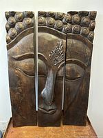 Front view of all three carved wood panels arranged to form Buddha face on table surface