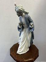 Front and side view of the King Balthasar Nao Lladro porcelain figurine on a wooden stand, showing detailed turban, beard, and flowing robes.