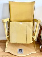 Front view of gold vinyl stadium seat folded upright on wooden base, showing seat number tag and overall condition