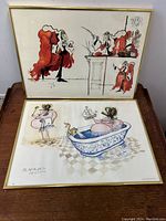 Pair of framed Ronald Searles art prints resting on a wooden surface, showing the artworks clearly.