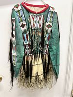 Full frontal view of jacket hanging on hanger showing beadwork panels, collar and fringe