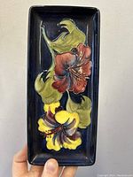 Front view of rectangular dark blue ceramic pen tray with yellow and red hibiscus motif