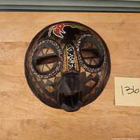 Front view of hand-carved wooden African mask with beadwork decorations and carved geometric shapes.