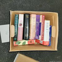 Top-down view of a box containing 8 Christian themed books and one small boxed item.