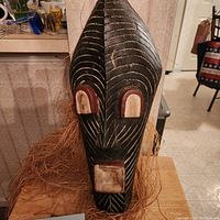 Frontal view of the wooden Congo Kifwebe mask showing painted geometric linear designs and natural fiber fringe.