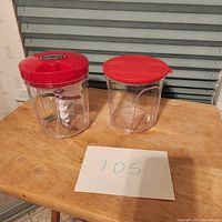 Two clear plastic containers with red lids on a wood surface, one with internal blade and pull string mechanism, the other an extra container.