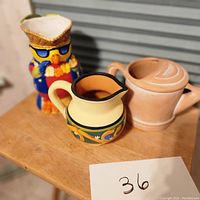Photo of three ceramic pitchers: owl-shaped, decorative yellow, and watering can-shaped.