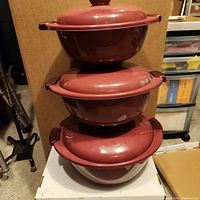 Three stacked mauve/maroon insulated bowls with lids, showing size variation and matching lids with handles.