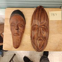 Two medium-sized wooden African masks placed on a wooden surface, displaying the front face details and size comparison.