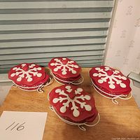 Photo of four red mini casserole dishes with lids and white snowflake design, placed on white metal stands on a wooden table.