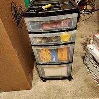 Side view of the black plastic 4-drawer storage unit filled with office supplies.