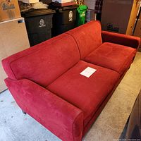 Front three quarter view of the red fabric sofa showing seat cushions and armrests with paper on seat.