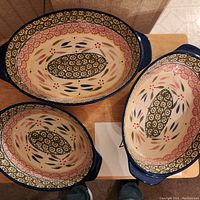 Top view of 3 nested oval casserole dishes showing floral and vine interior patterns with blue and red accents.