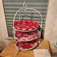 Full view of the three-tiered pie stand with plates stacked in the white metal rack, placed on wooden surface.