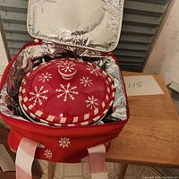 Red Temptations casserole bowl with lid inside the red insulated carrier bag, showing snowflake pattern and checked trim on the lid and bowl.