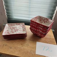 Four stacked square small plates and four stacked square bowls with red floral lace pattern on cream background and red scalloped edges.