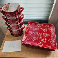 Set of 4 red soup bowls with white floral lace design stacked in black metal rack alongside 4 matching square plates.