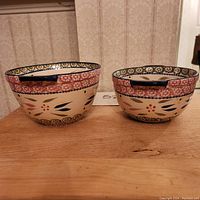Two ceramic mixing bowls, front view on wooden surface, showing decorative floral patterns and handles.
