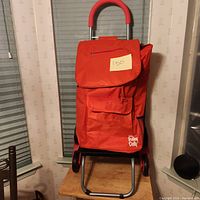 Full view of red folding trolley dolly with handle and stair climbing wheels placed on a chair indoors.