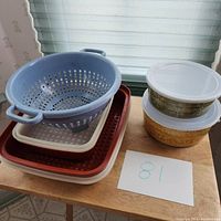 Photo of 2 Tupperware Season & Serve containers with lids and decorative patterns, 2 rectangular trays with lids, and a blue colander on a wooden surface.