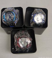 Three sport watches in black metal boxes, wrapped in protective plastic, showing faces and designs clearly.
