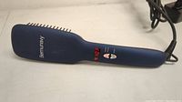 Dark blue Bermunavy hair straightener brush with digital temperature display illuminated, showing a red numeric reading, photographed from the front angle on a white surface.