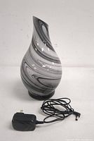 Full view of the ceramic lamp shade, showing the black and white swirl pattern, teardrop shape, and power adapter coiled beside it.