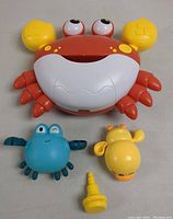 Front view of crab bath bubbler, blue crab toy, yellow giraffe toy, and yellow nozzle on a white surface.