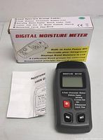 Photo of the digital moisture meter device next to its user manual and package box.