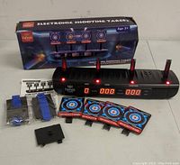 Electronic shooting target system displayed outside box showing base unit, four circular targets on poles, mounting accessories, and power indicator lights.