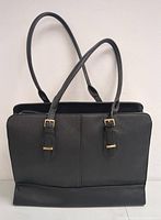 Front view of the black handbag showing double shoulder straps with gold-tone buckles and smooth faux leather texture