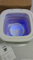 Top view of the mini folding washing machine showing interior and blue LED light.