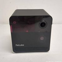 Front view of a black cube-shaped Petcube Camera showing the camera lens and speaker grille with Petcube logo.