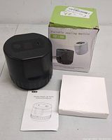 Photo showing the black handheld portable sealing machine YZ-80, its instruction manual, and a white accessory box alongside the product box with green and white design.