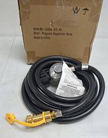 Coiled black propane regulator hose with yellow cap and metal regulator, alongside safety and warning labels, presented out of box.