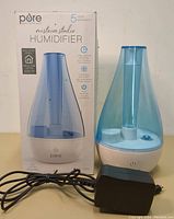 Photo showing humidifier with blue translucent water tank, white base, and power adapter alongside original box.