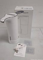 Photo showing white YIKHOM sensor soap dispenser with curved spout, USB cable, user manual, and adhesive pads on white surface.