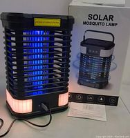 Black solar mosquito lamp lit with UV and orange bottom lights, plugged in with USB cable, shown with instruction sheet and product box