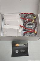 Open box showing three Luminoodle LED strip lights with power connectors arranged neatly inside the box, along with a folded instruction manual.