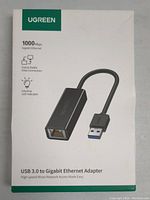 Photo of the packaging box showing the adapter image, branding, and specifications like 1000 Mbps speed, fast and stable data connection, and LED indicator.