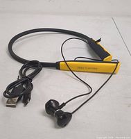 Yellow and black wireless Bluetooth neckband headphones with built-in earbuds and a USB charging cable coiled beside it.