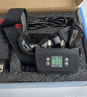 Close-up photo of the black adjustable pet collar with LED screen and control buttons placed inside foam packaging.