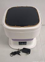 Top view of closed portable laundry machine showing black lid with gold-colored hinges on white ribbed body.