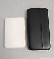 Two portable power banks, one white and one black, front view with LED indicators visible.