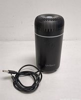 Front view of black UrrSaw USB air diffuser with power button and USB cable attached, showing overall shape and design.