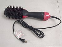 All-in-one hair dryer with black and red styling brush head, showing power cord and plug.