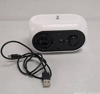 Front view of white automatic dog barking device with control dials and USB cable placed beside it.