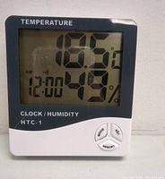 Front view of the digital clock showing temperature 18.5°C, humidity 49%, time 12:00 AM. Clock labeled HTC-1 with buttons MODE, ADJ, MEMORY.